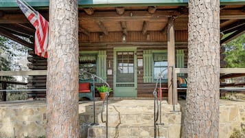 A rustic wooden cabin with a stone porch, a green door, and an American flag.