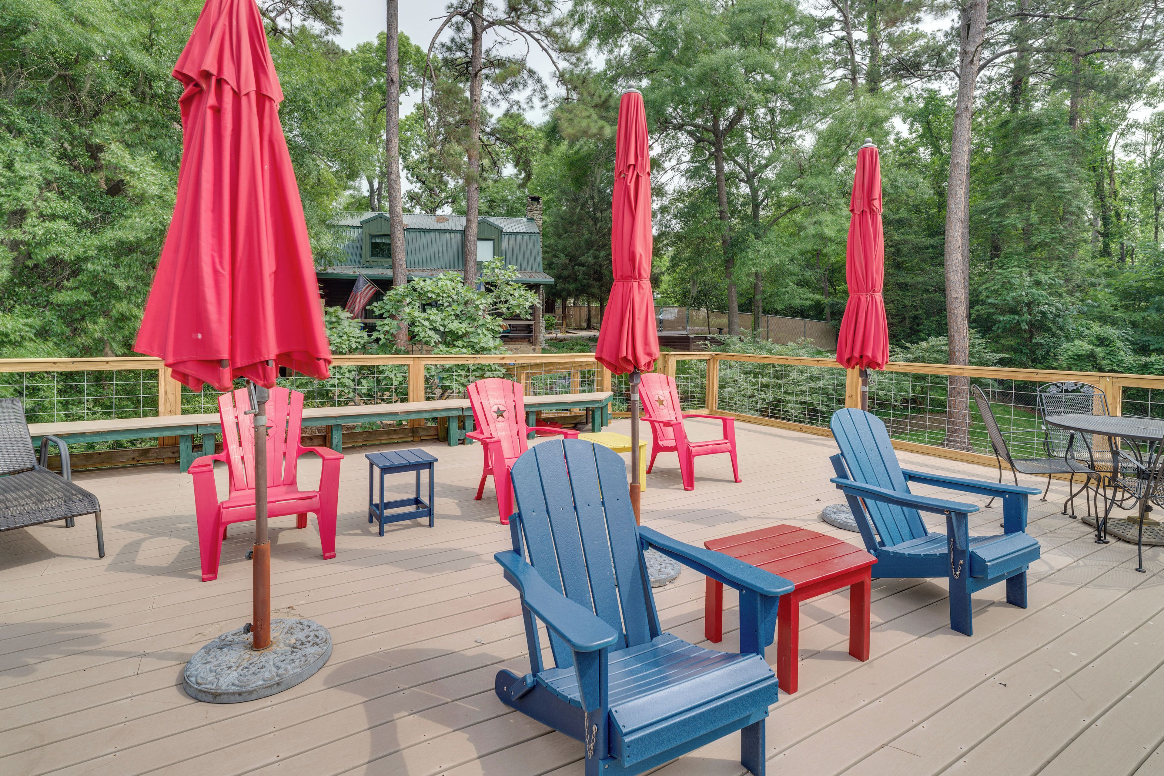 A deck with Adirondack chairs, red umbrellas, and a table.