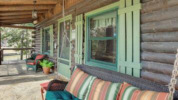 A log cabin with a porch, wicker furniture, and a hanging lantern.