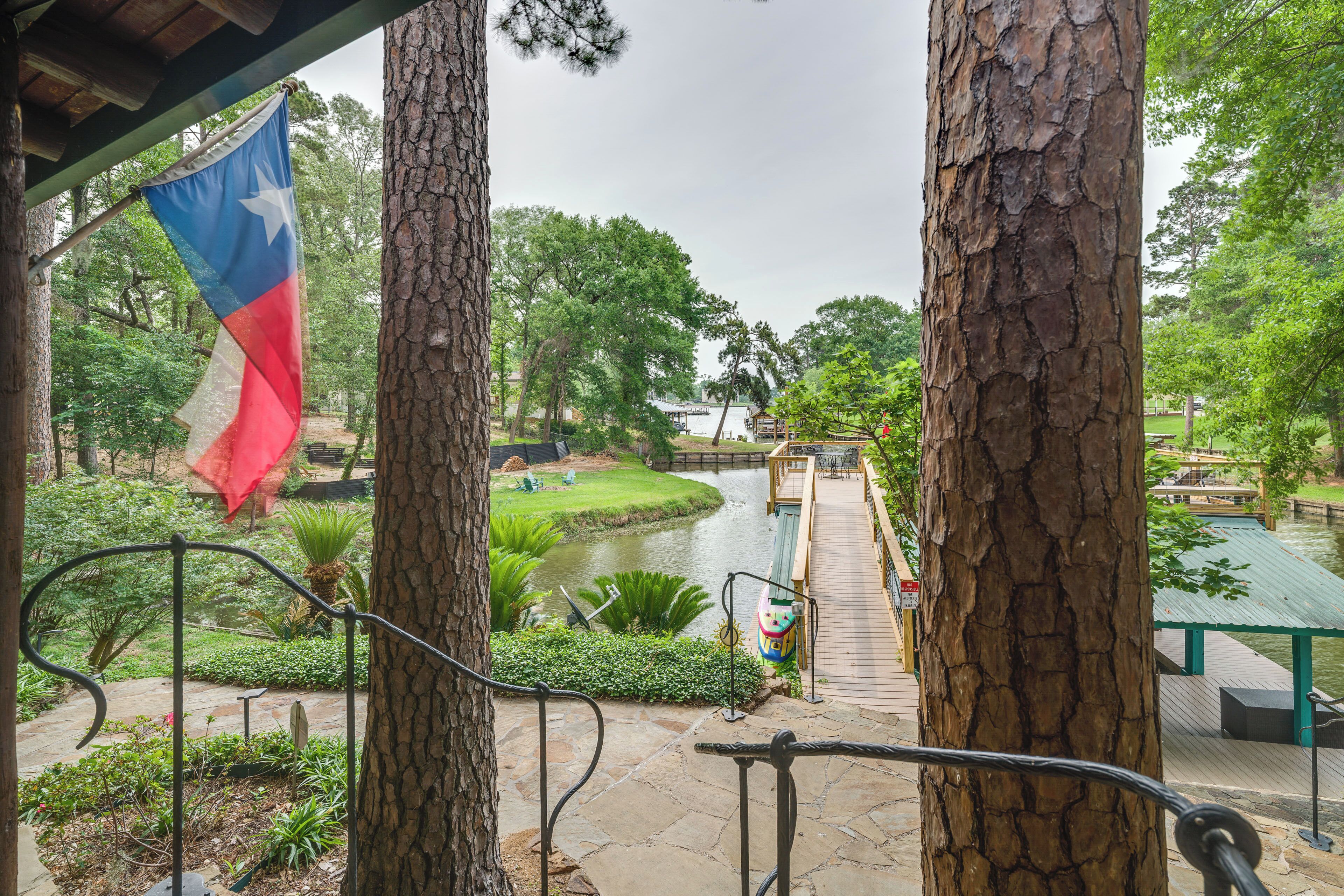 A park with a river, trees, a flag, and a wooden bridge.