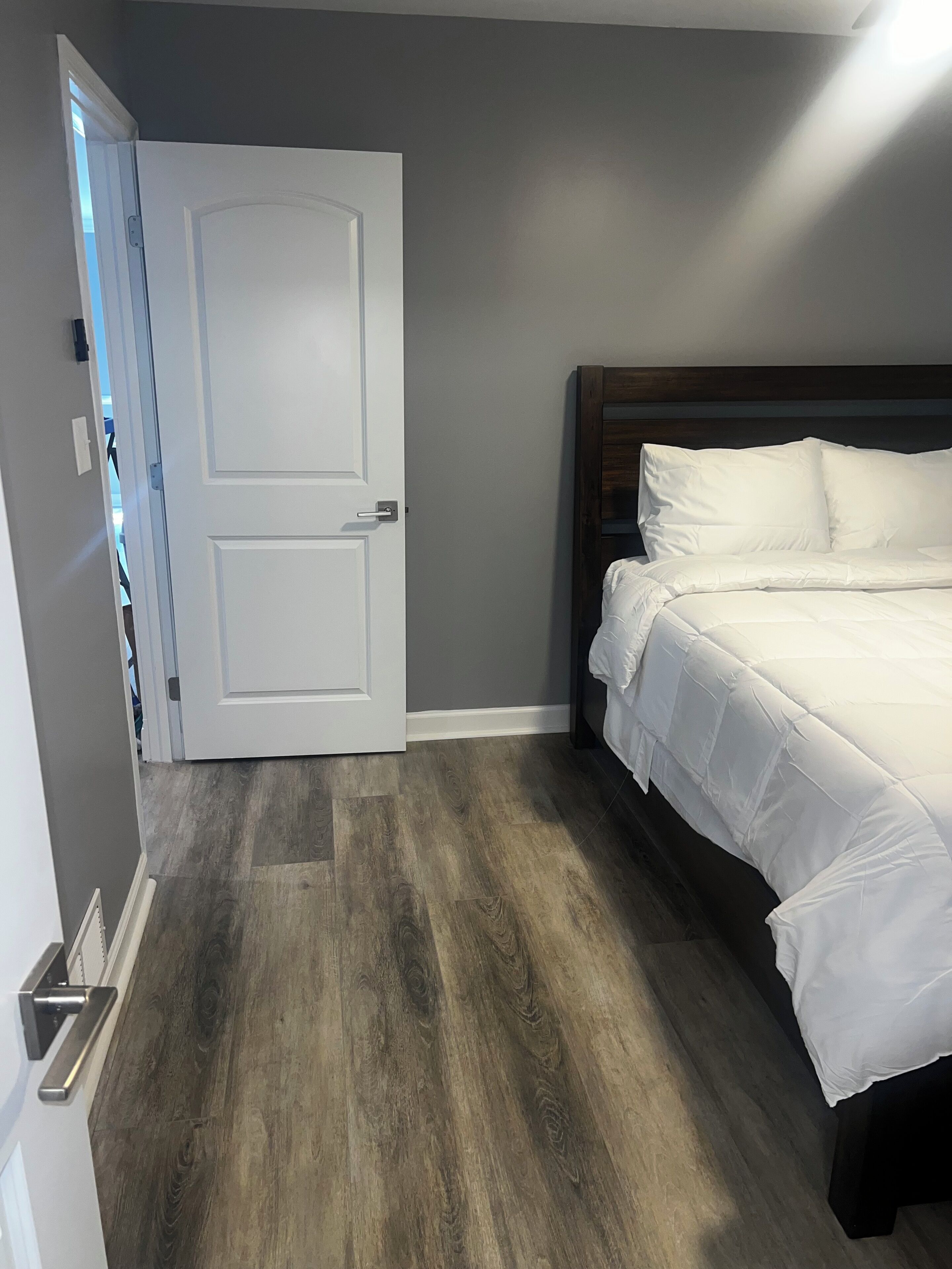 A bedroom with a wooden floor, a white door, and a bed with white bedding.