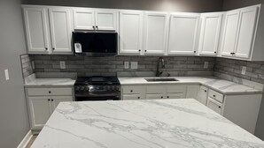 A kitchen with white cabinetry, a stainless steel stove, a microwave, and a marble countertop. - Elevated three master suites with jet tub, large kitchen, full of amenities (Camden)