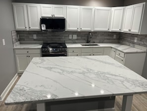 A kitchen with white cabinetry, a stainless steel stove, a microwave, and a marble countertop. - Elevated three master suites with jet tub, large kitchen, full of amenities (Camden)