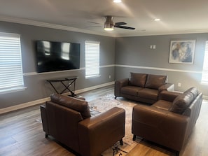 A living room with a brown leather sofa set, a flat-screen TV mounted on the wall, and a ceiling fan. - Elevated three master suites with jet tub, large kitchen, full of amenities (Camden)