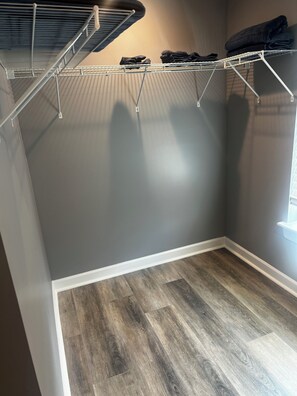 A room with a grey wall, a wooden floor, and a metal drying rack with folded clothes. - Elevated three master suites with jet tub, large kitchen, full of amenities (Camden)