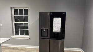 A modern kitchen with a stainless steel refrigerator, a window with white frames, and a wooden floor. - Elevated three master suites with jet tub, large kitchen, full of amenities (Camden)