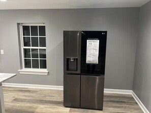 A modern kitchen with a stainless steel refrigerator, a window with white frames, and a wooden floor. - Elevated three master suites with jet tub, large kitchen, full of amenities (Camden)
