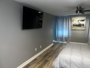 A bedroom with a bed, a mounted TV, a ceiling fan, and a window with curtains. - Elevated three master suites with jet tub, large kitchen, full of amenities (Camden)