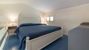 Een slaapkamer met een bed, nachtkastjes, een raam en een trap.