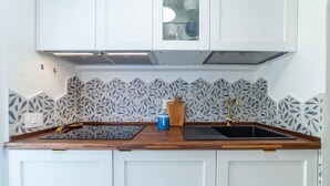 Een keuken met witte kastjes, een zwart aanrecht, een blauwe waterkoker en een houten snijplank.