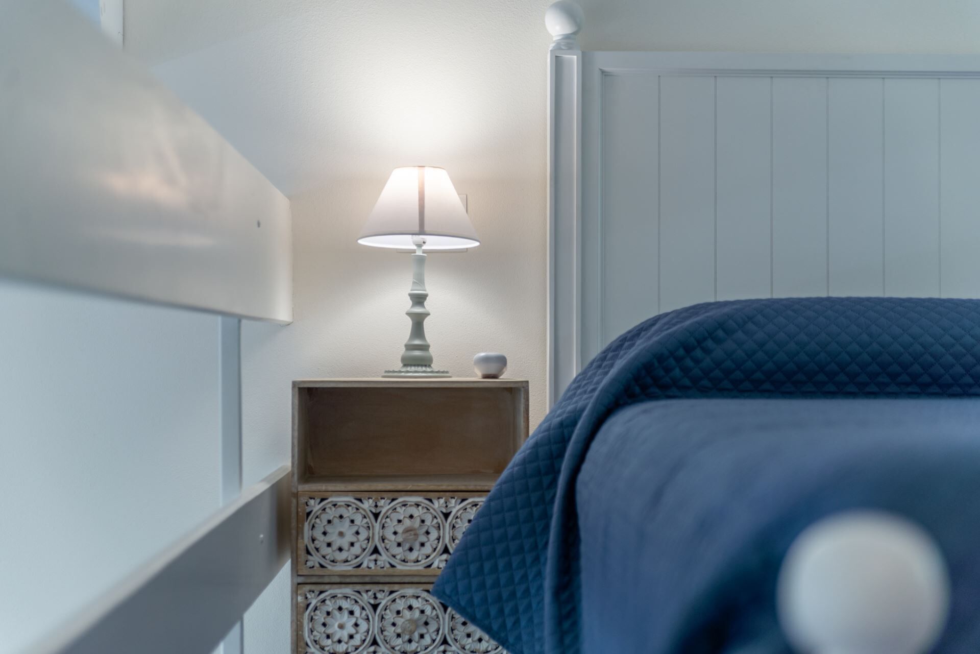 Een slaapkamer met een bed, een nachtkastje met een lamp en een decoratief wandpaneel.