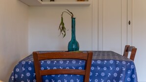Een eettafel met een blauwe tafelkleed, een groene vaas met een plant, en een houten stoel.