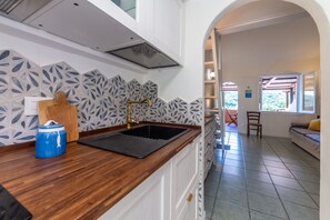 A kitchen with a black sink, white cabinets, and patterned backsplash. - Il Portolano 15 - Goelba (Porto Azzurro)