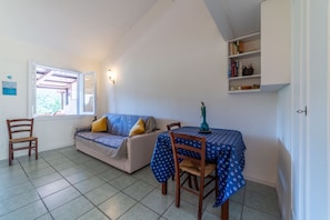 Quarto com sofá, mesa de jantar com toalha, cadeira, estante e janela.