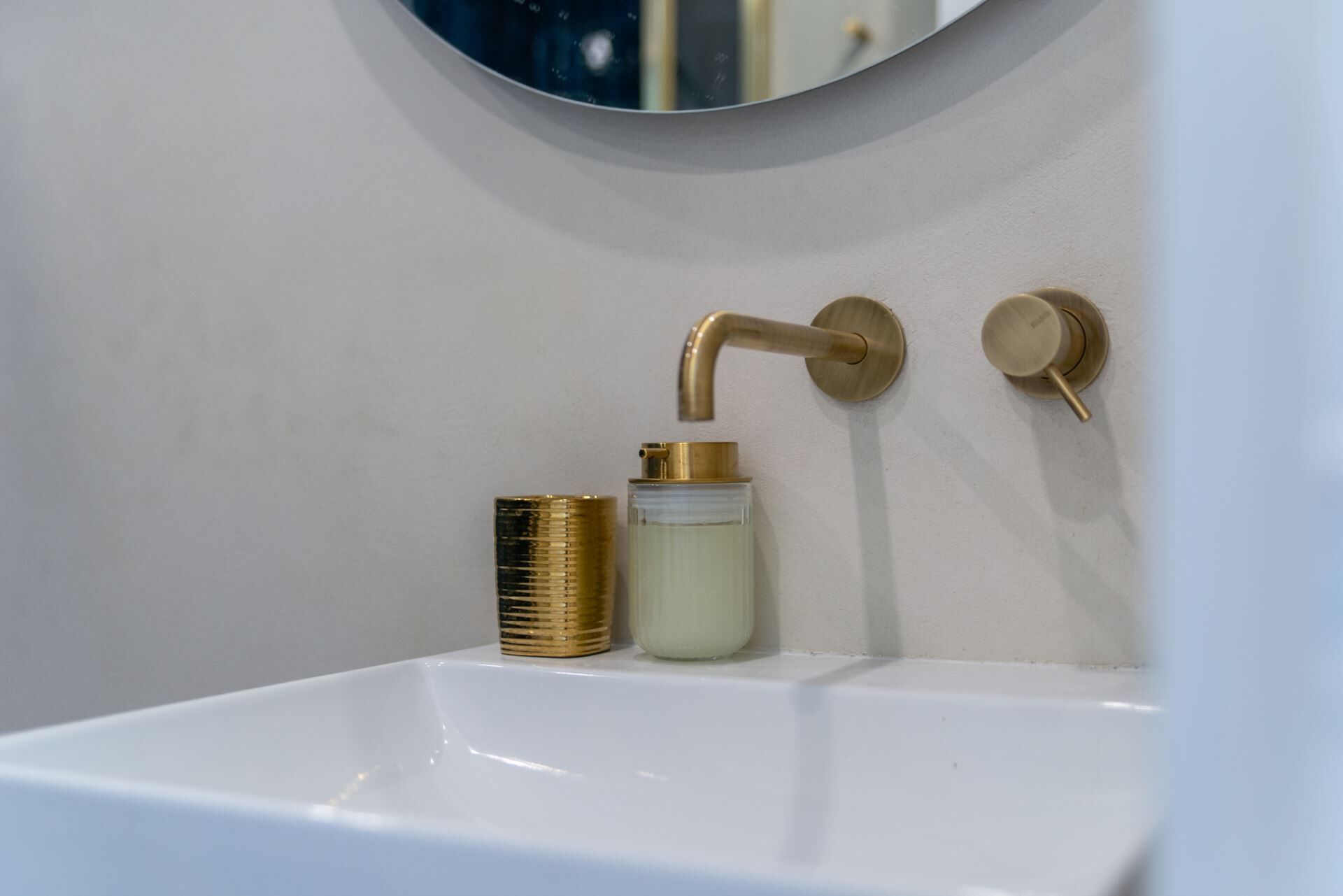 Un lavabo de salle de bain avec un robinet doré, un distributeur de savon et un miroir au-dessus.