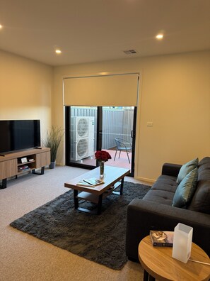 A living room with a flat-screen TV, a coffee table with books, a sofa, and a small side table with a book and a white object. - New large 3BR,3bathrms townhouse in Gunghalin, mountain views,central location (Gungahlin)