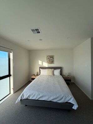A bedroom with a large bed, a nightstand, a wall-mounted artwork, and a window. - New large 3BR,3bathrms townhouse in Gunghalin, mountain views,central location (Gungahlin)
