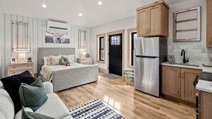 Un apartamento moderno con una cama, un sofá, una cocina con armarios de madera y un refrigerador.