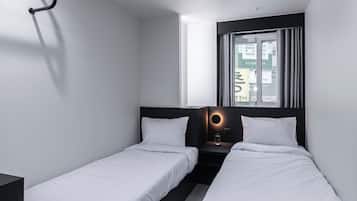 Habitación de hotel moderna con dos camas individuales, un escritorio, una mesita y una ventana con cortinas.
