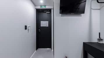 Un pasillo con una puerta negra, un televisor montado, un extintor y un dispensador de gel antibacterial.