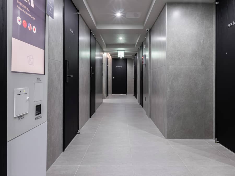 Un pasillo moderno con un cartel de registro sin llave, un detector de incendios y una escalera que sube a otro nivel.