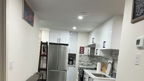 A modern kitchen with a central island, stainless steel appliances, and a black rug leading to the dining area. - 3 BdR Suite in Calgary - Enjoy Rockies, Banff, Lake Louise, Dinosaur museum (Calgary)