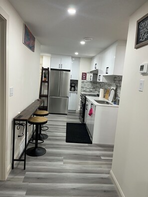 A modern kitchen with a central island, stainless steel appliances, and a black rug leading to the dining area. - 3 BdR Suite in Calgary - Enjoy Rockies, Banff, Lake Louise, Dinosaur museum (Calgary)