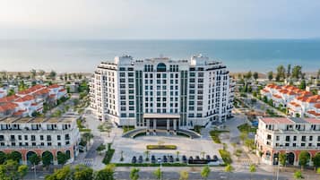 A multi-story hotel with a central courtyard, surrounded by residential buildings, overlooking a beach.