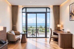 A hotel room with a balcony, a desk, a sofa, and a small table with a vase of flowers. - Tra Co Long Beach Hotel & Resort (Mong Cai)