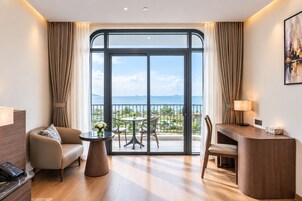 A hotel room with a balcony, a desk, a sofa, and a small table with a vase of flowers.