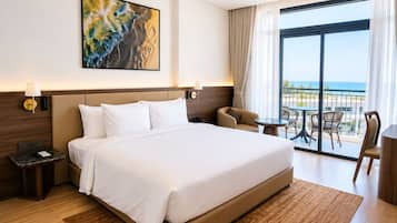 Habitación de hotel con una cama grande, un escritorio, una silla, un balcón con vistas y un cuadro en la pared.