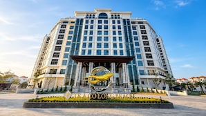 A large hotel with a central entrance, multiple floors, and a distinctive golden sign. - Tra Co Long Beach Hotel & Resort (Mong Cai)