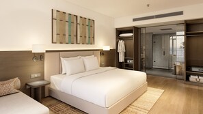 Habitación de hotel moderna con una cama grande, mesitas de noche, vestidor y vista al baño.