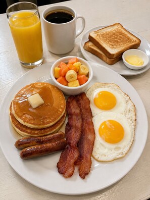 A breakfast plate with pancakes, bacon, sausages, eggs, toast, and a fruit bowl. - Hospedaje valeria (Granada)