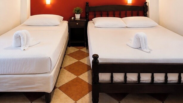 A hotel room with two single beds, a nightstand, a painting on the wall, and a tiled floor. - Hospedaje valeria  (Granada)