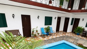 A swimming pool with a blue border, surrounded by a checkered floor pattern, and a green lawn area. - Hospedaje valeria  (Granada)