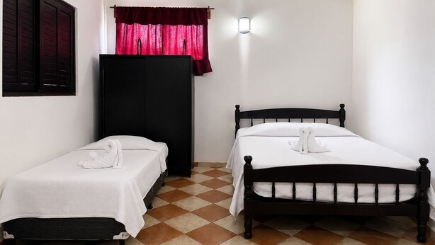 Une chambre avec deux lits simples, une armoire, un ventilateur de plafond et une fenêtre avec des rideaux.
