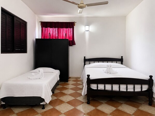 A room with two single beds, a wardrobe, a ceiling fan, and a window with curtains.