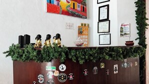 A reception desk with a wooden finish, adorned with various badges and certificates, and a colorful painting above it. - Hospedaje valeria  (Granada)