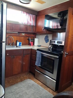 Una cocina compacta con armarios de madera, un lavamanos de acero inoxidable, un microondas y un horno.