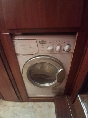 Lavadora de carga frontal con perillas de control y una etiqueta, ubicada en un gabinete de madera.