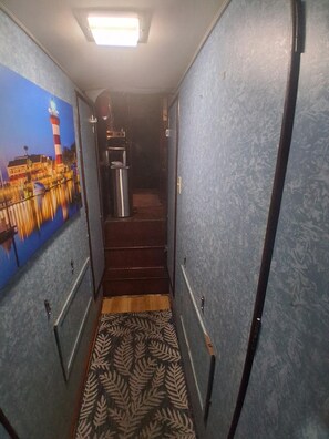 Um corredor estreito com paredes estampadas, uma escada e uma lixeira.