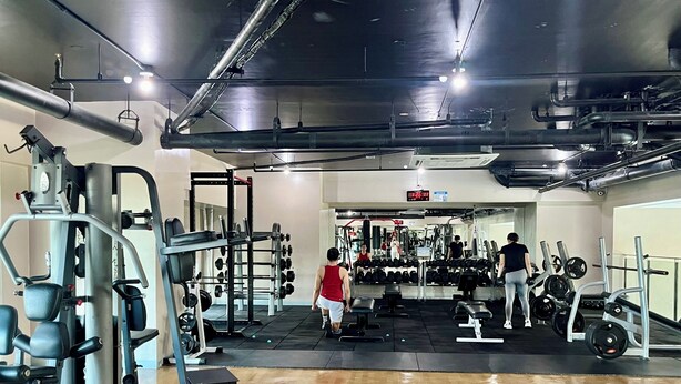 Ein Fitnessstudio mit verschiedenen Trainingsgeräten, darunter Kraftgeräte und Kurzhanteln.