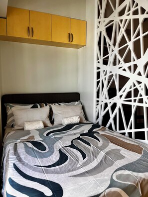 A bed with a patterned bedspread, a headboard, and a yellow cabinet above it. - Modern Beacon Makati Studio • City View • Pool • Fast Wi-Fi • Sleeps 3 (Makati City)