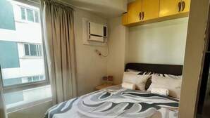 Ein Hotelzimmer mit einem Bett, einer Klimaanlage, einem Fenster mit Vorhängen und Blick auf Gebäude.