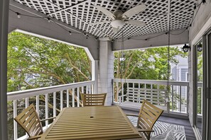 Un área de estar al aire libre techada con mesa y sillas, ventilador de techo y vista a los árboles a través de las ventanas.