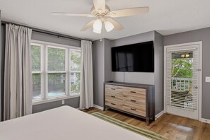 Un dormitorio con cama, cómoda, ventilador de techo, televisión y ventana con persianas.