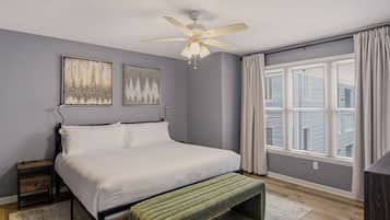 A bedroom with a bed, a nightstand, a bedside table, a ceiling fan, and a window with blinds.