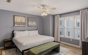 Un dormitorio con cama, mesita de noche, ventilador de techo y ventana con persianas.