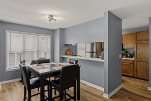 A modern kitchen with a built-in refrigerator, wooden cabinets, and a dining area with a marble table and black chairs.